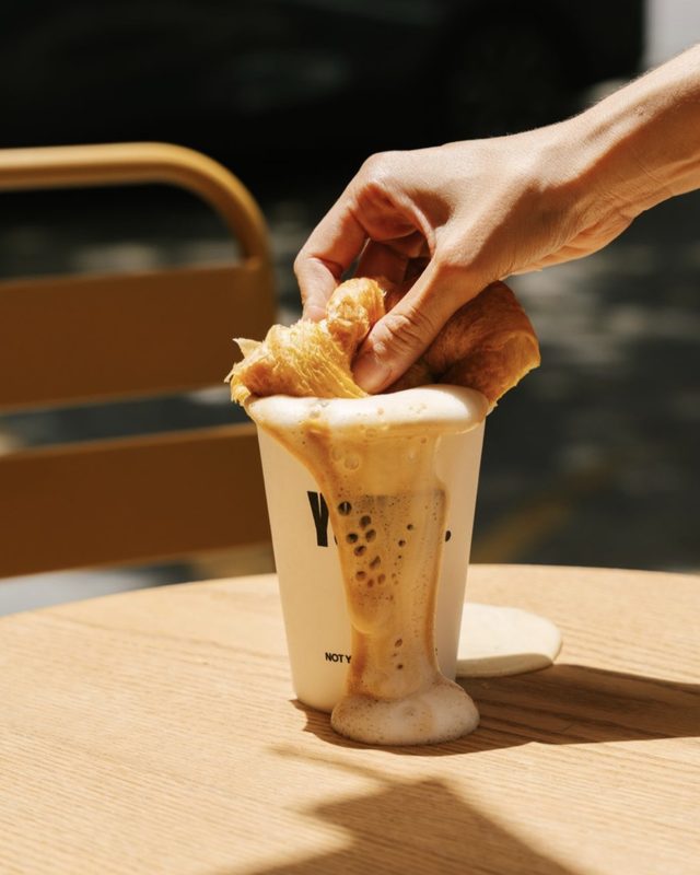A croissant dipped into a YOUNG Coffee cup